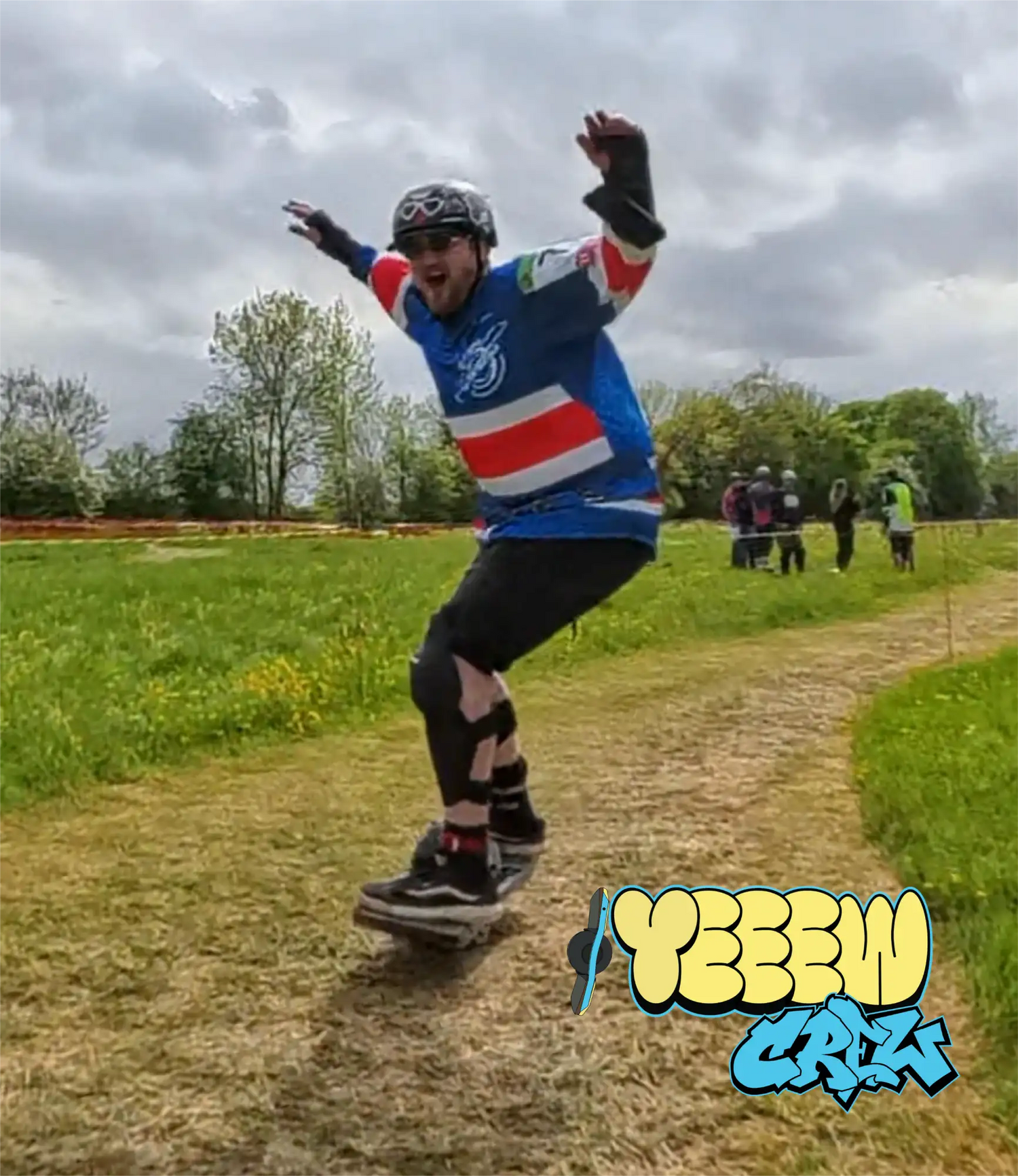 A person wearing a blue, red, and white striped jersey with black knee pads and gloves is riding a longboard on an outdoor path.