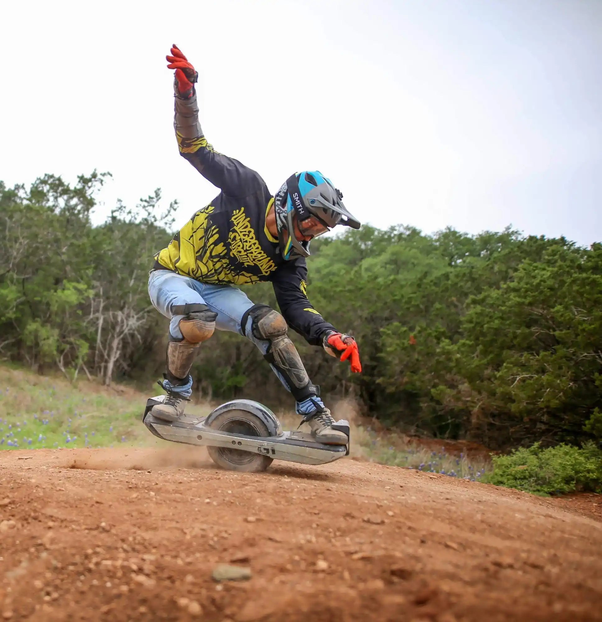 A person riding a one-wheeled electric skateboard on a dirt path.